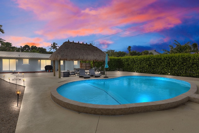 pool at dusk with a gazebo, area for grilling, and a patio area