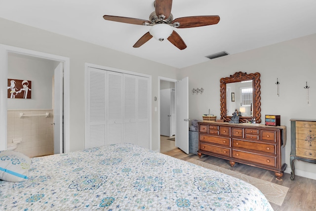 bedroom with light hardwood / wood-style flooring, ceiling fan, tile walls, connected bathroom, and a closet