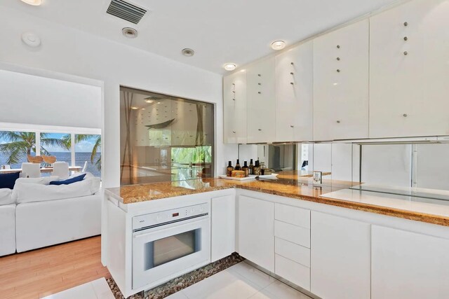 kitchen with visible vents, white cabinets, oven, and light stone countertops