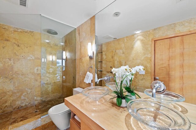 bathroom with tile walls, vanity, toilet, and tiled shower