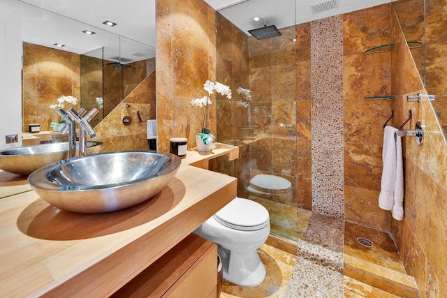 full bathroom featuring visible vents, a walk in shower, toilet, vanity, and tile walls