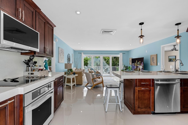 kitchen featuring light tile patterned flooring, a breakfast bar, sink, decorative light fixtures, and appliances with stainless steel finishes