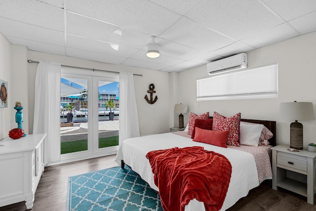 bedroom featuring dark hardwood / wood-style flooring, access to outside, a drop ceiling, and a wall unit AC