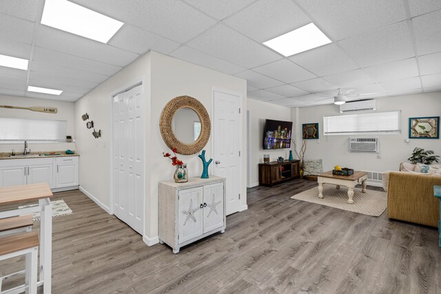 interior space with an AC wall unit, sink, a drop ceiling, and light hardwood / wood-style floors