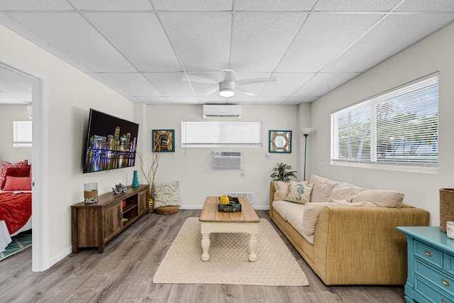 living room featuring a drop ceiling, a wall mounted AC, and light wood-type flooring