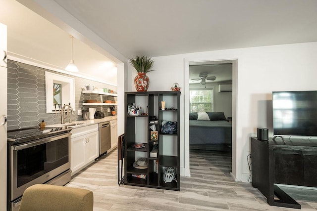 kitchen with pendant lighting, sink, white cabinetry, stainless steel appliances, and light wood-type flooring