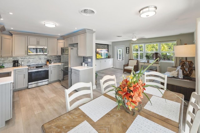 kitchen featuring stainless steel appliances, gray cabinets, light wood-type flooring, and decorative backsplash