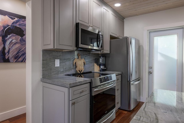 kitchen with dark wood-type flooring, appliances with stainless steel finishes, gray cabinetry, backsplash, and light stone counters