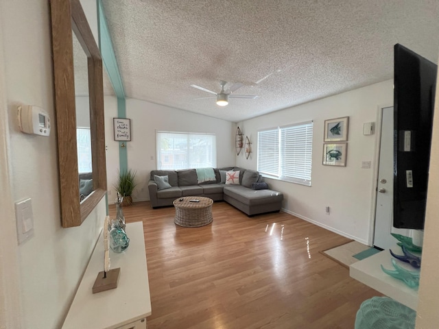 living room with ceiling fan, a textured ceiling, and light wood-type flooring