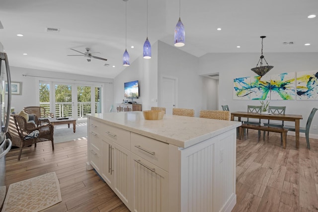 kitchen with vaulted ceiling, hanging light fixtures, a center island, ceiling fan, and light wood-type flooring