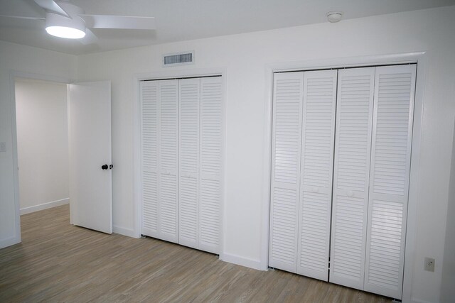 unfurnished bedroom featuring multiple closets, ceiling fan, and light hardwood / wood-style floors