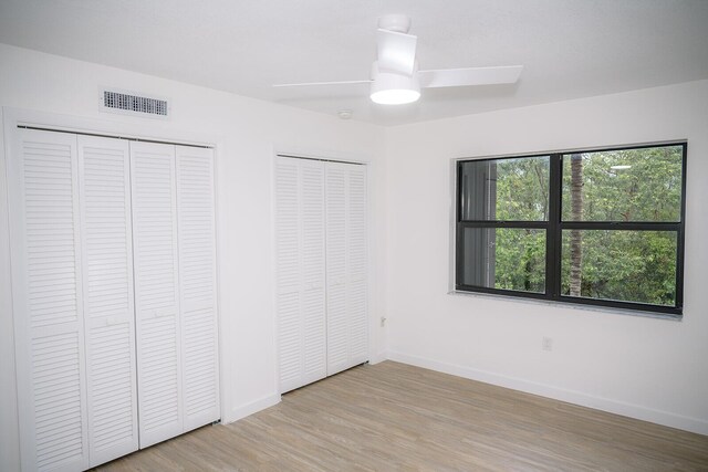 unfurnished bedroom featuring multiple closets, ceiling fan, and light wood-type flooring