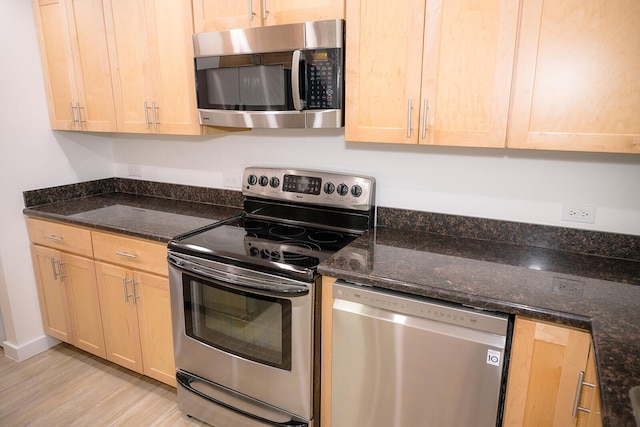 kitchen with stainless steel appliances, light brown cabinetry, light hardwood / wood-style flooring, and dark stone countertops