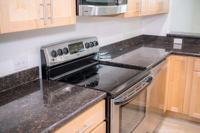 kitchen with dark stone countertops, light wood-type flooring, stainless steel appliances, and light brown cabinets