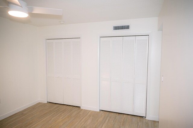 unfurnished bedroom featuring ceiling fan, two closets, and light wood-type flooring