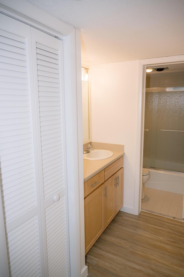 full bathroom featuring vanity, hardwood / wood-style floors, enclosed tub / shower combo, and toilet