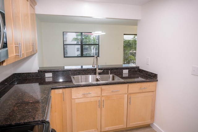 kitchen with light brown cabinetry, sink, hanging light fixtures, and dark stone countertops