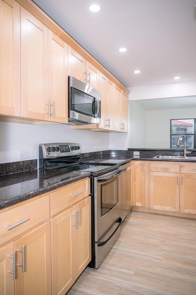 kitchen with sink, light brown cabinets, dark stone countertops, stainless steel appliances, and light hardwood / wood-style floors