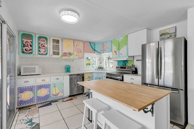 kitchen with a breakfast bar area, white cabinetry, light tile patterned floors, appliances with stainless steel finishes, and decorative backsplash