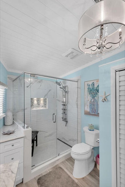 bathroom with an enclosed shower, wood-type flooring, ornamental molding, vanity, and a notable chandelier