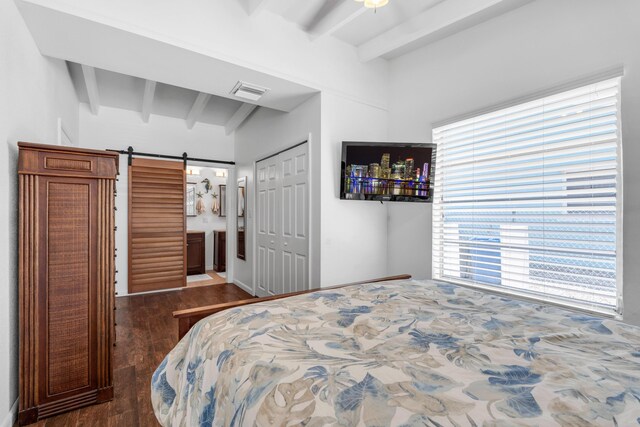 bedroom with beam ceiling, ensuite bath, dark hardwood / wood-style flooring, a closet, and a barn door