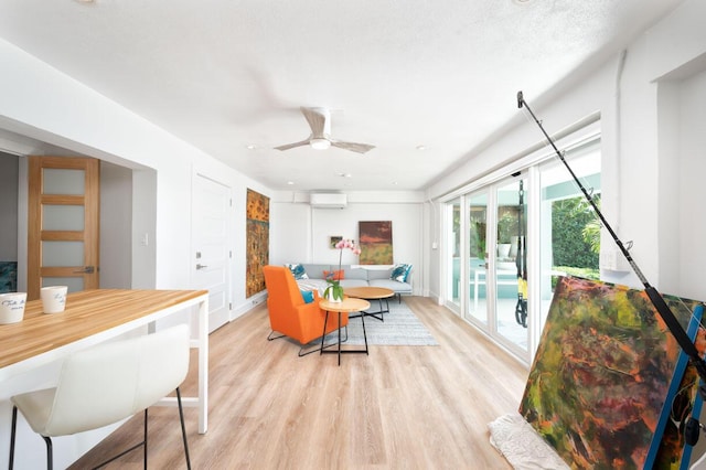 living room featuring a textured ceiling, a wall unit AC, ceiling fan, and light wood-type flooring