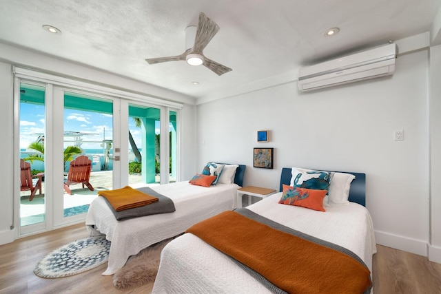 bedroom with an AC wall unit, access to exterior, ceiling fan, light wood-type flooring, and french doors