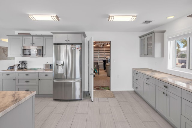 kitchen with gray cabinets, light stone countertops, and appliances with stainless steel finishes