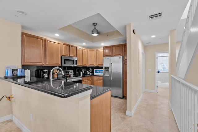 kitchen with kitchen peninsula, dark stone counters, ceiling fan, a tray ceiling, and stainless steel appliances