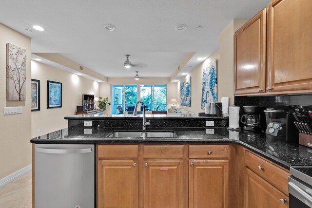 kitchen with appliances with stainless steel finishes, sink, dark stone countertops, and kitchen peninsula