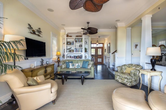 living area featuring ornate columns, ceiling fan, crown molding, and wainscoting