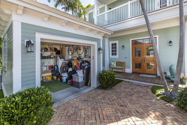 property entrance featuring decorative driveway, french doors, a balcony, and an attached garage