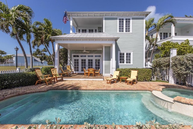 back of house featuring metal roof, a pool with connected hot tub, a ceiling fan, a standing seam roof, and a patio area