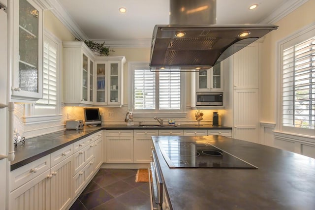 kitchen with white cabinets, ornamental molding, stainless steel microwave, dark countertops, and glass insert cabinets