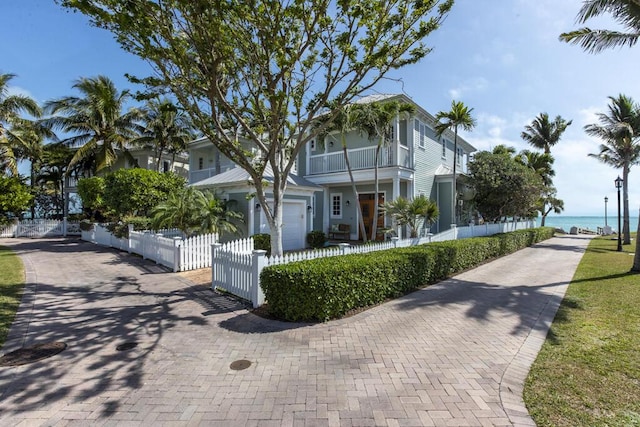 view of front facade featuring a water view, a fenced front yard, a garage, and decorative driveway