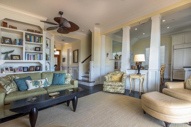 living room featuring a ceiling fan, wainscoting, decorative columns, and stairs