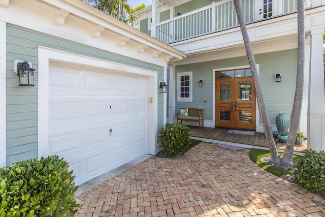 doorway to property with a balcony, an attached garage, decorative driveway, and french doors