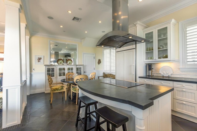 kitchen featuring visible vents, white cabinetry, dark countertops, island exhaust hood, and glass insert cabinets