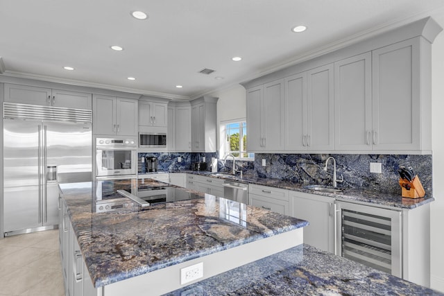 kitchen with dark stone countertops, built in appliances, wine cooler, and backsplash