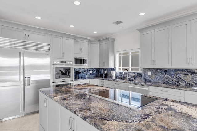 kitchen featuring tasteful backsplash, sink, dark stone countertops, ornamental molding, and built in appliances