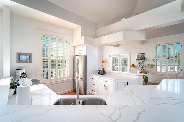 kitchen with sink, stainless steel fridge, white cabinetry, light stone counters, and kitchen peninsula