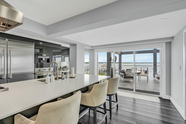 kitchen featuring extractor fan, dark hardwood / wood-style floors, a breakfast bar, stainless steel built in refrigerator, and a water view