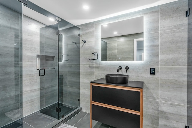 bathroom featuring tile patterned flooring, vanity, tile walls, and a shower with shower door