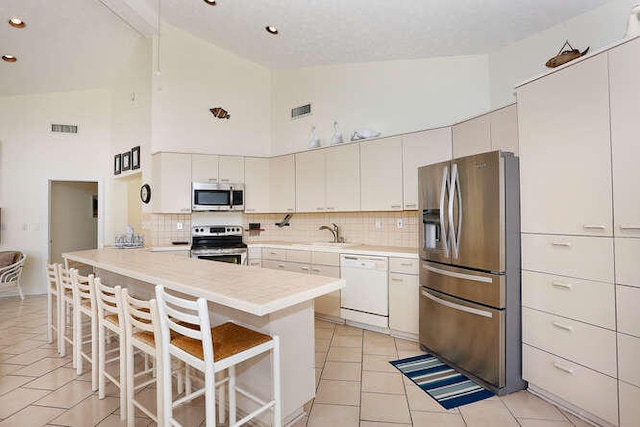 kitchen with visible vents, a peninsula, high vaulted ceiling, tasteful backsplash, and appliances with stainless steel finishes
