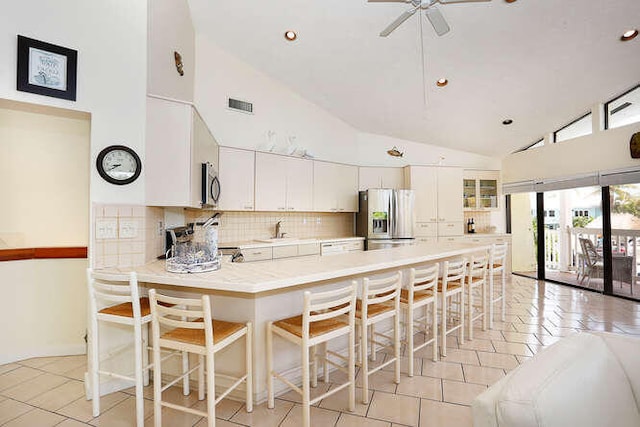 kitchen with a peninsula, light tile patterned flooring, high vaulted ceiling, light countertops, and appliances with stainless steel finishes
