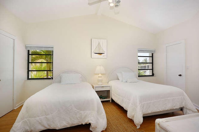bedroom with vaulted ceiling with beams, wood finished floors, and multiple windows
