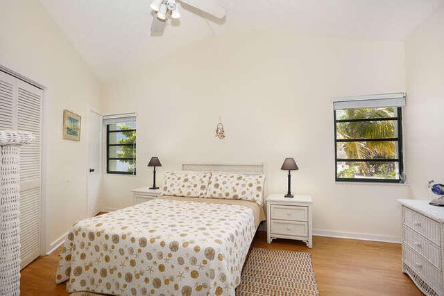 bedroom with a ceiling fan, wood finished floors, baseboards, a closet, and lofted ceiling
