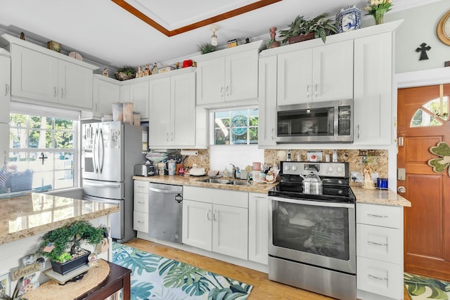 kitchen with appliances with stainless steel finishes, a sink, light stone countertops, and white cabinets