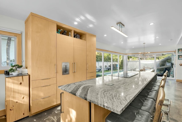 kitchen featuring light brown cabinetry, concrete floors, decorative light fixtures, and light stone countertops