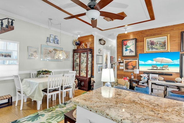 kitchen featuring light wood-style flooring, ornamental molding, a ceiling fan, wooden walls, and light stone countertops